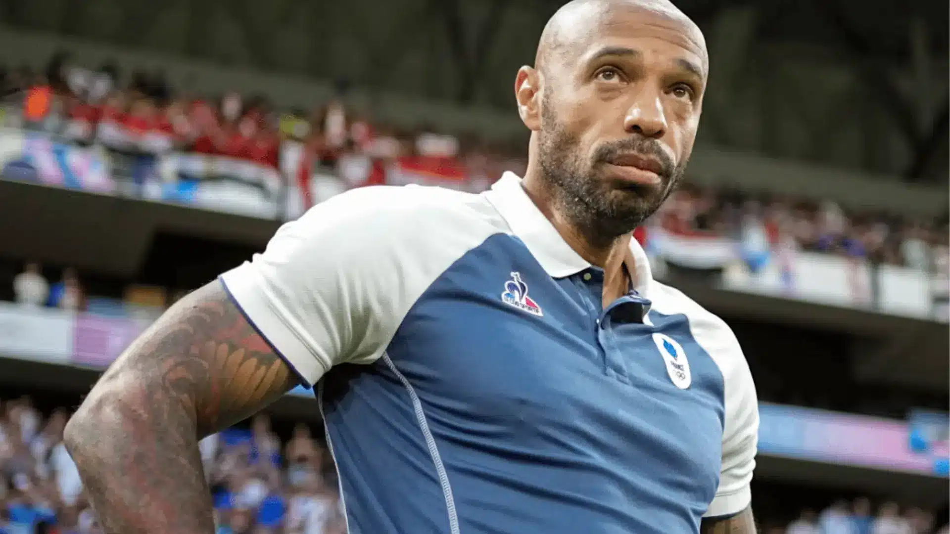 Thierry Henry stands beside the field wearing a France Olympic soccer team polo shirt.