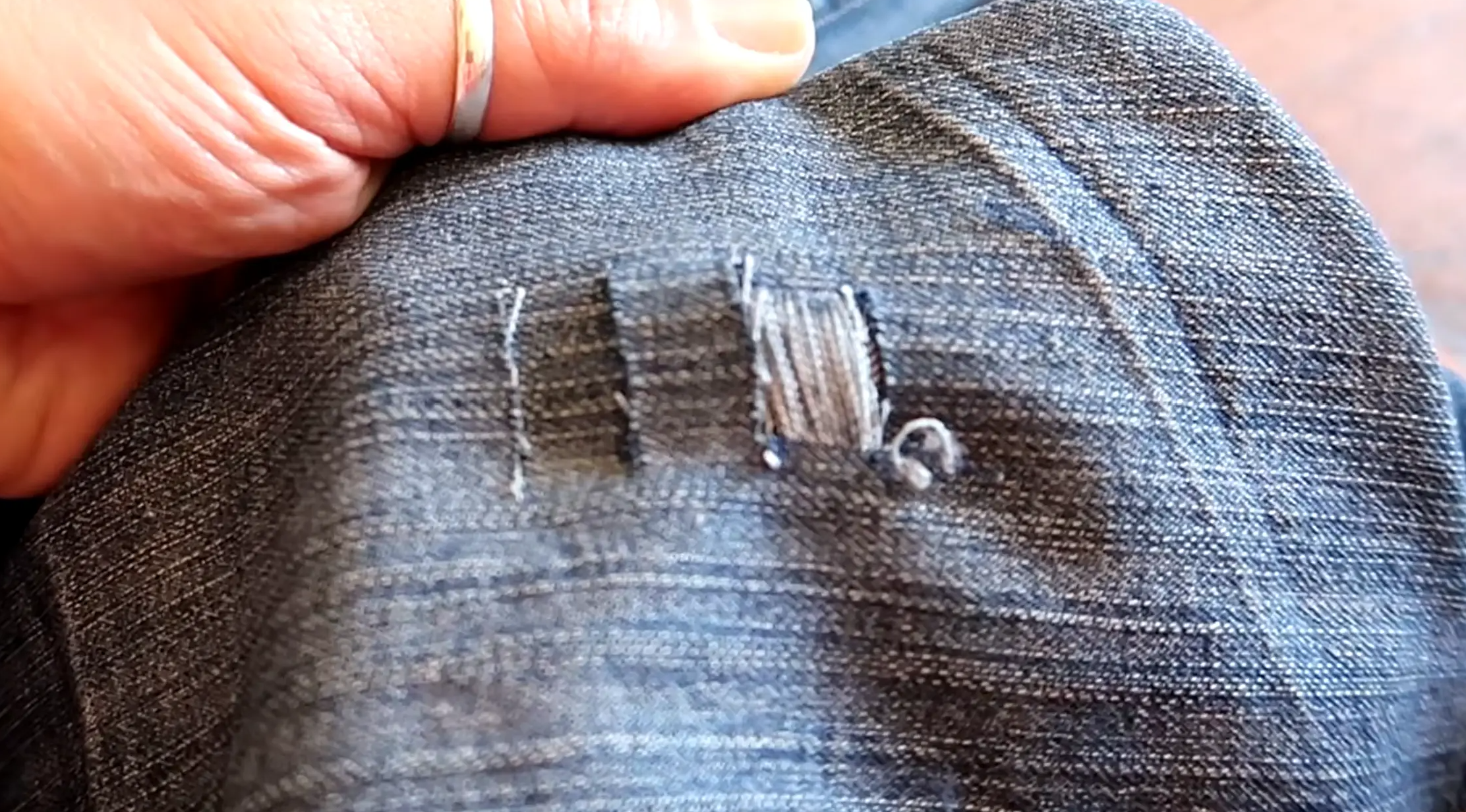 Tweezers pulling blue denim threads from a freshly cut distressed jeans section
