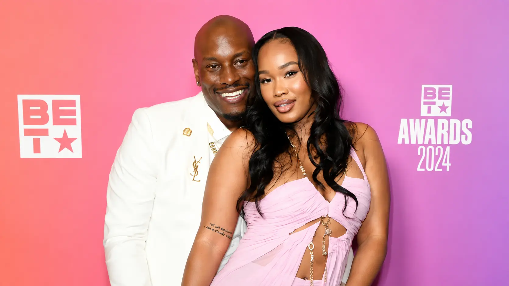 Tyrese Gibson and Zelie Timothy posing at BET Awards 2024 backdrop with tyrese gibson in white suit and Zelie Timothy in pink dress during red carpet event