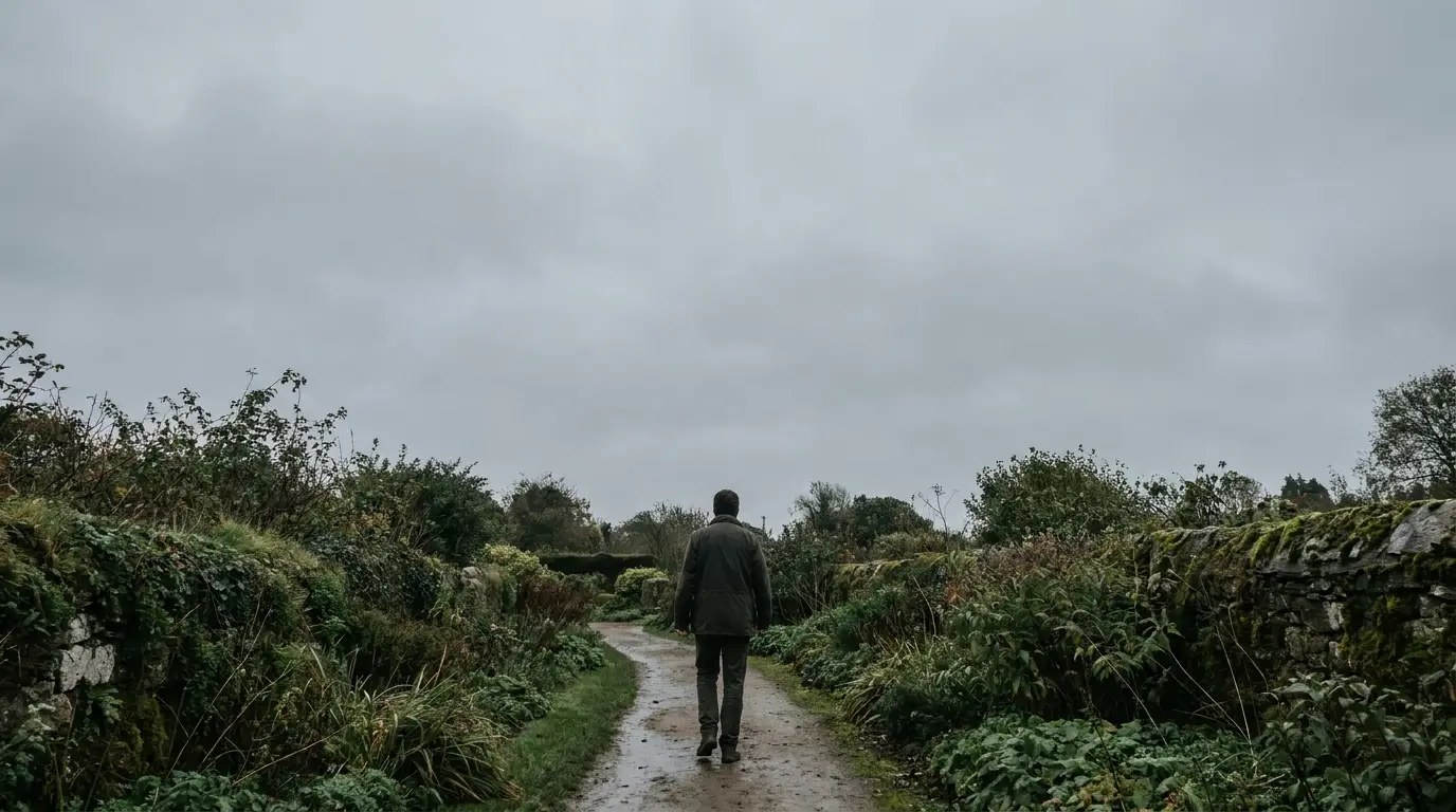 Man walking on a narrow path through a lush, overgrown garden under cloudy skies