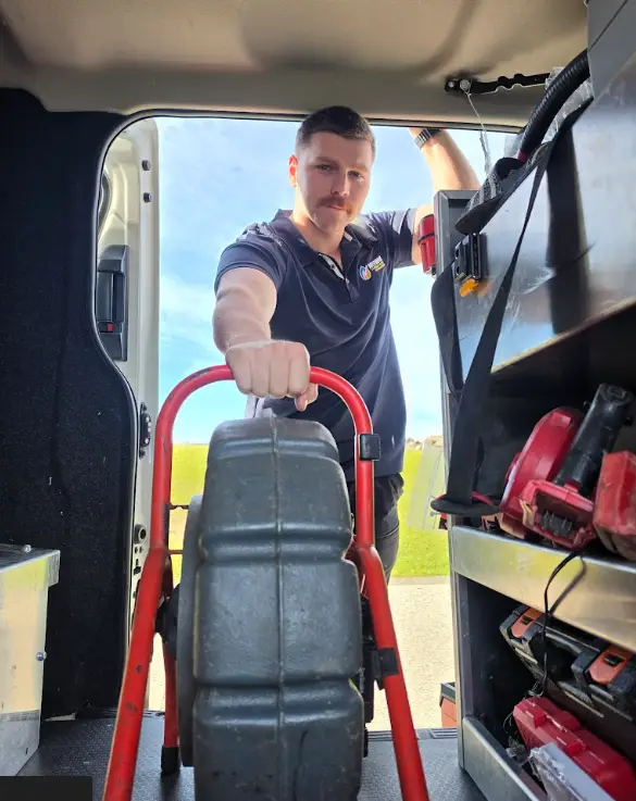 Man holding red hand truck inside vehicle with tool shelves and blue sky outside