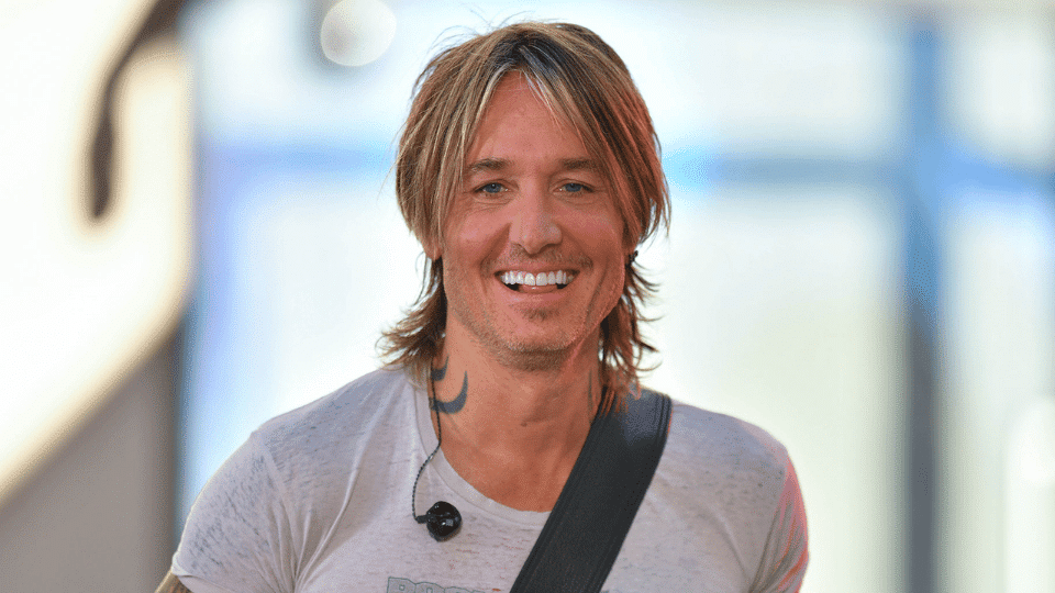 Keith Urban smiling while wearing a casual t-shirt and an in-ear monitor.