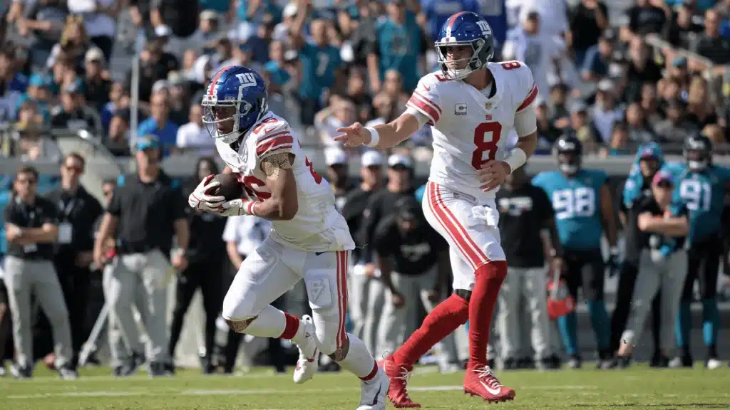 NFL running back taking a handoff from the quarterback during a live game, breaking into a run past the line of scrimmage.
