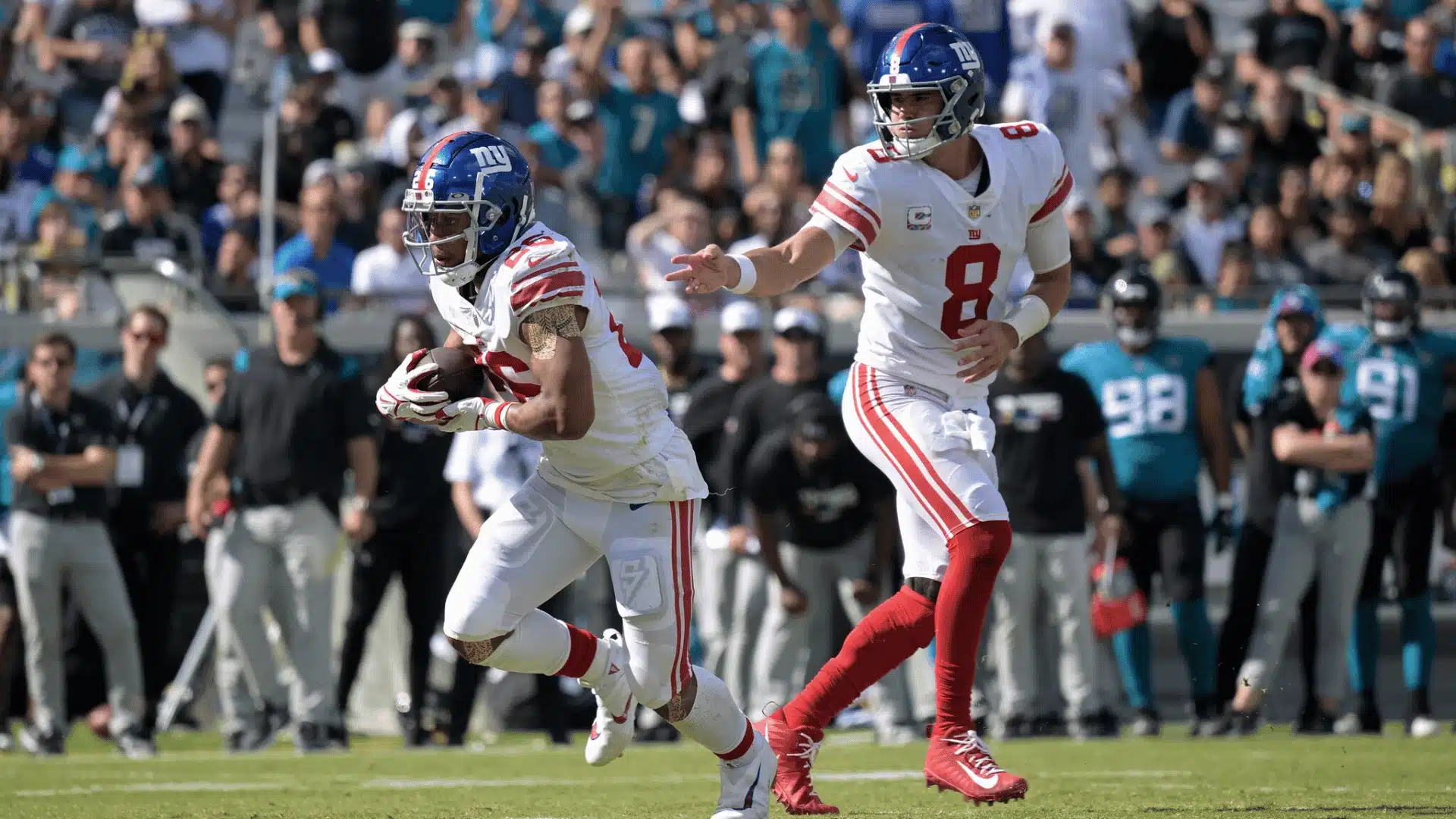 NFL running back taking a handoff from the quarterback during a live game, breaking into a run past the line of scrimmage.