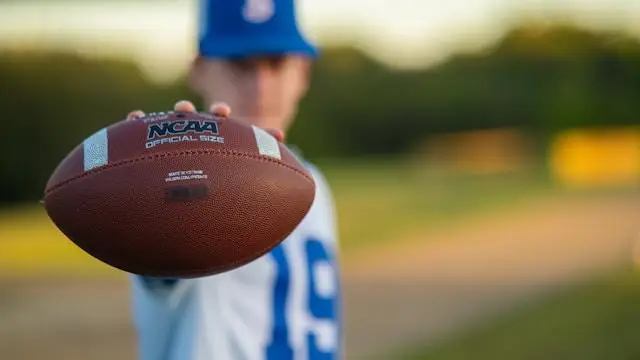 Blurred person holding a football towards the camera in a sunny outdoor setting