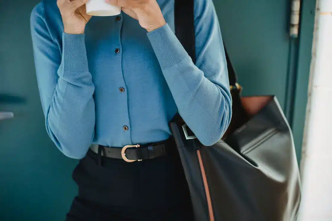 Person in blue sweater holding a coffee cup with a large black bag in an indoor setting