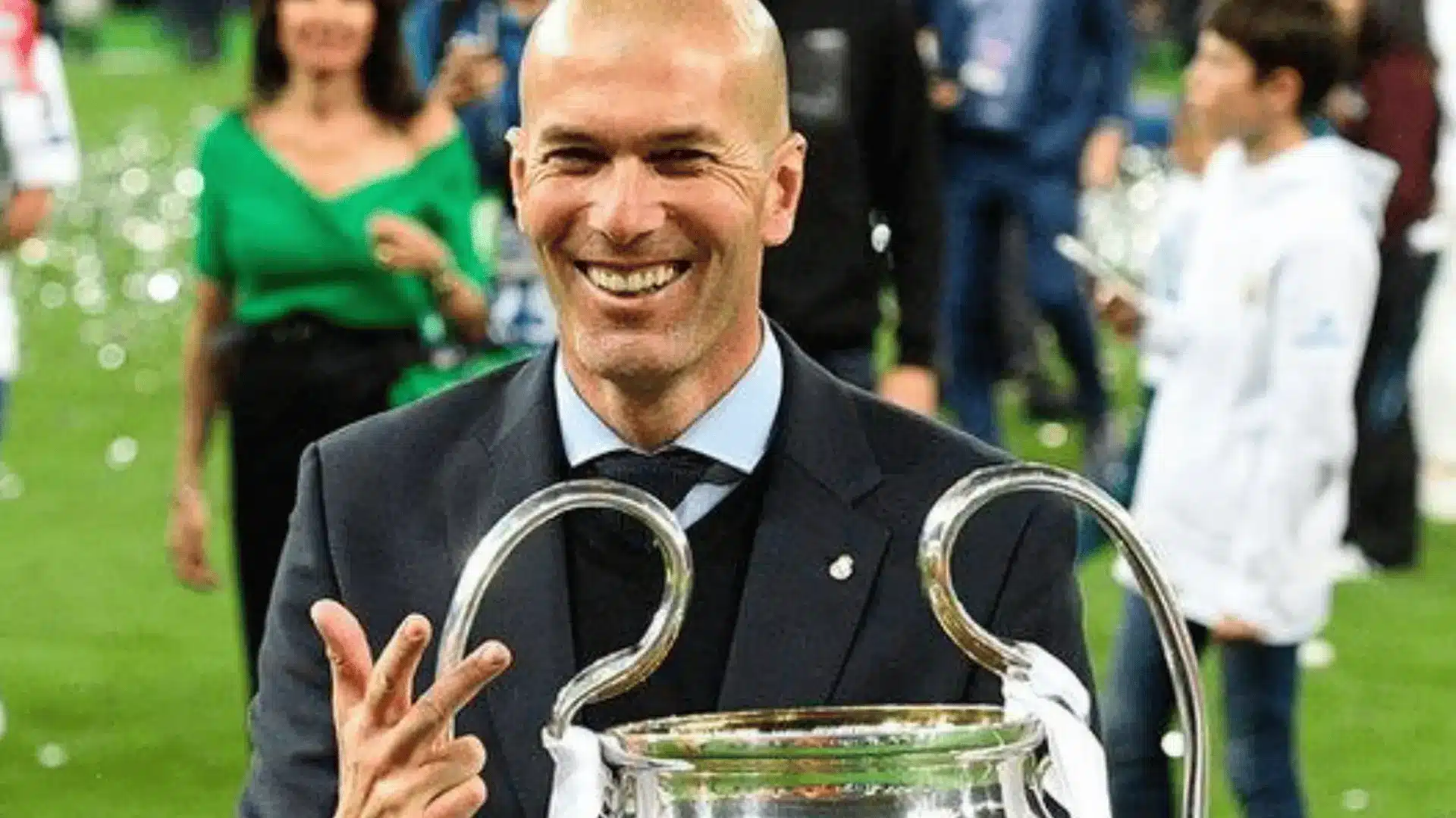 Zinedine Zidane smiles beside the UEFA Champions League trophy after winning as Real Madrid manager.