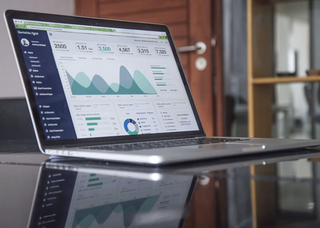 Laptop displaying analytics dashboard with graphs and charts on reflective desk in office setting