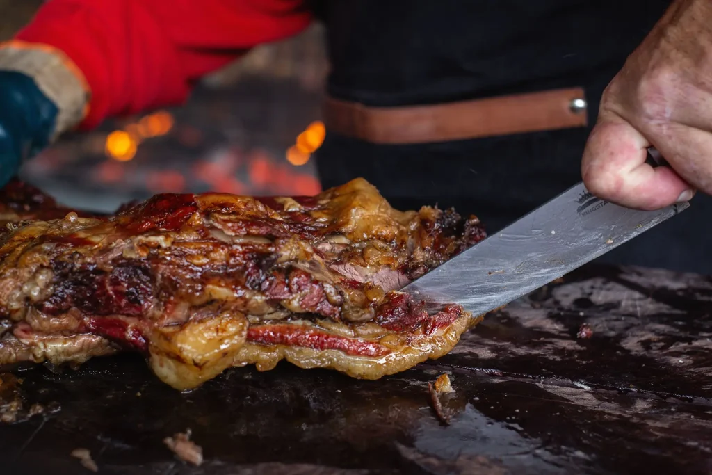 Grilled meat being sliced with a knife on a wooden cutting board