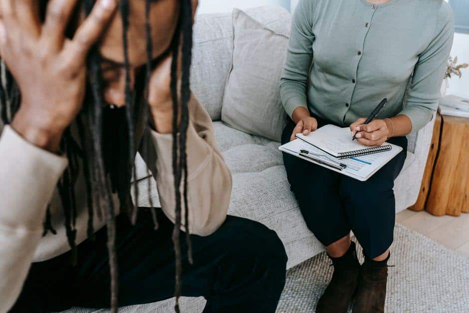 Therapist taking notes while listening to person on sofa in a cozy living room