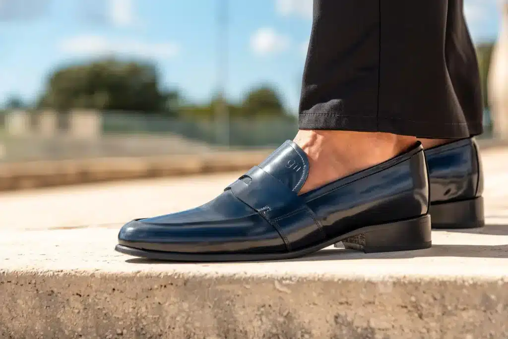 Shiny black leather loafers worn with black pants on outdoor stone steps