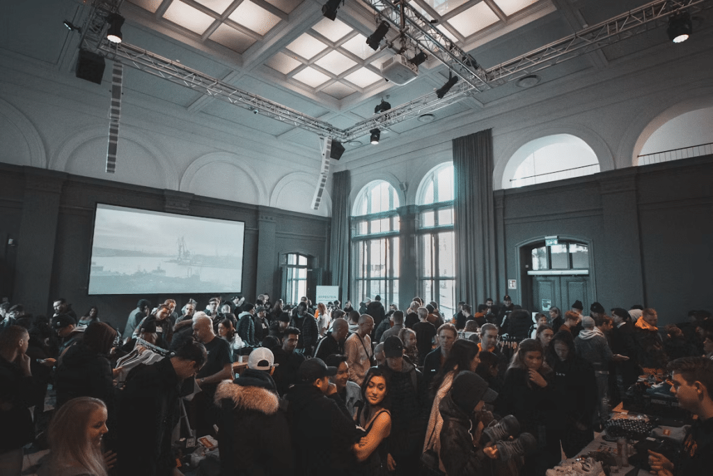 Crowd gathered at indoor event with large windows and hanging lights