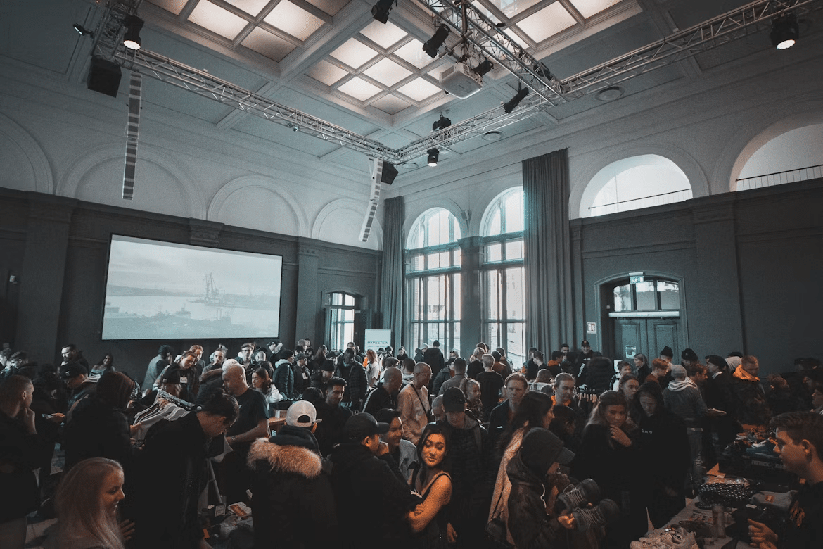 Crowd gathered at indoor event with large windows and hanging lights