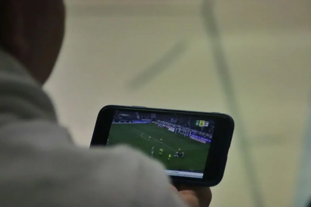 Person watching football match on smartphone screen indoors