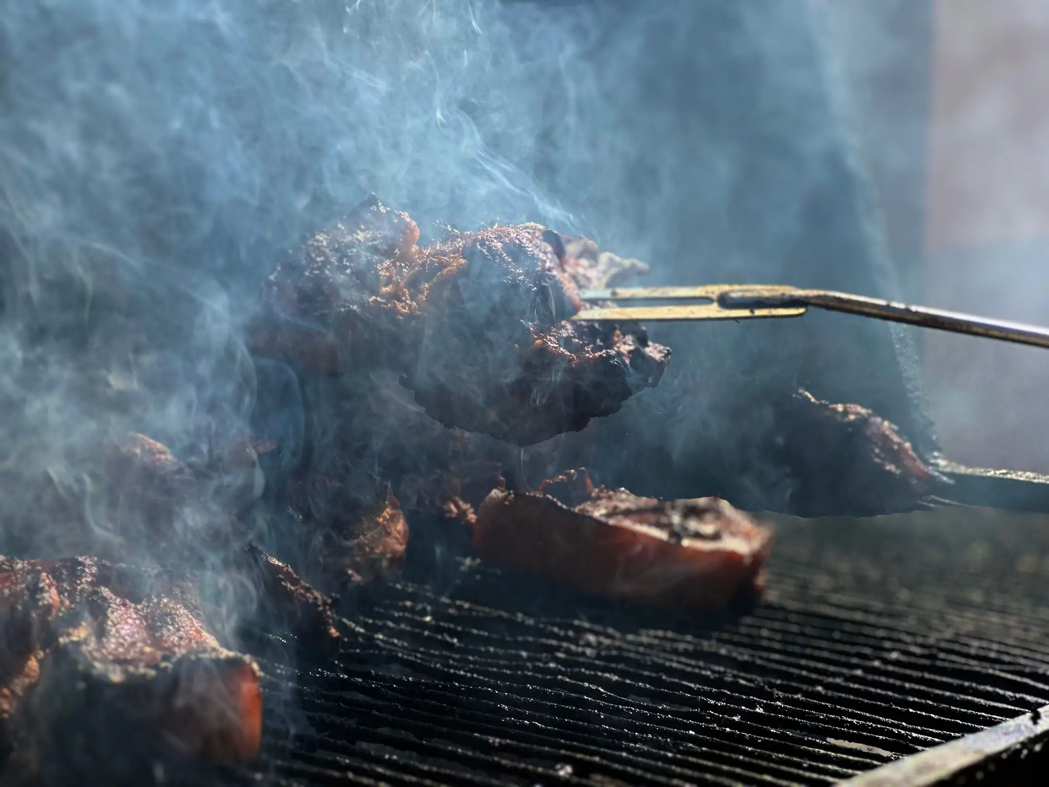 Barbecue ribs being grilled with smoke rising outdoors