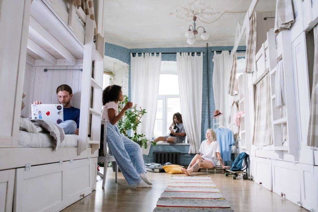 People relaxing and socializing in a bright shared living space with bunk beds and large windows