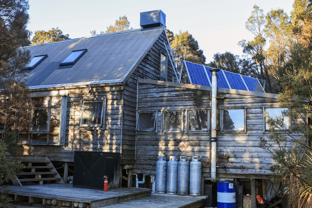 Wooden cabin with solar panels and gas cylinders in forested outdoor setting