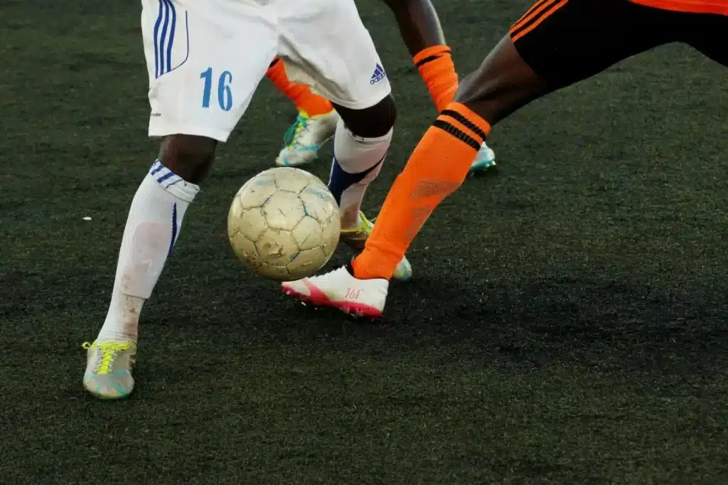 Soccer players competing for ball on dark turf field, wearing colorful jerseys and socks